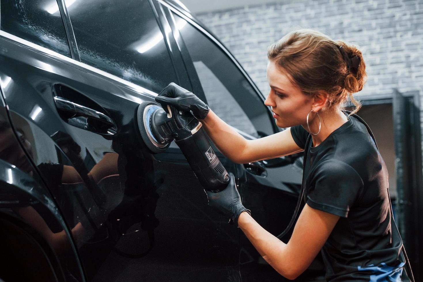 Polishing surface of vehicle. Modern black automobile get cleaned by woman inside of car wash station photo