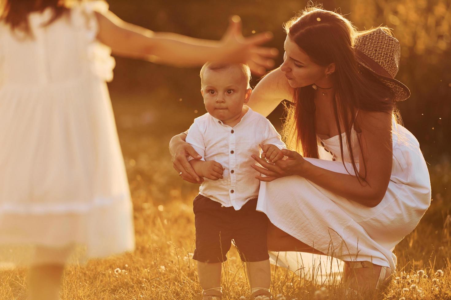 Happy family of mother, little son and daughter spending free time on the field at sunny day time of summer photo