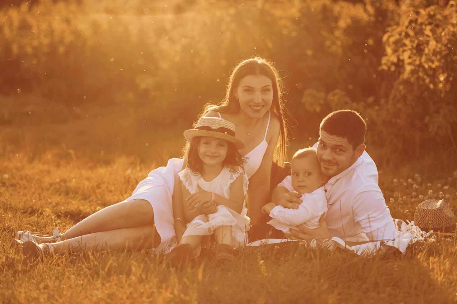 Sitting on the grass. Father, mother with daughter and son spending free time outdoors at sunny day time of summer photo