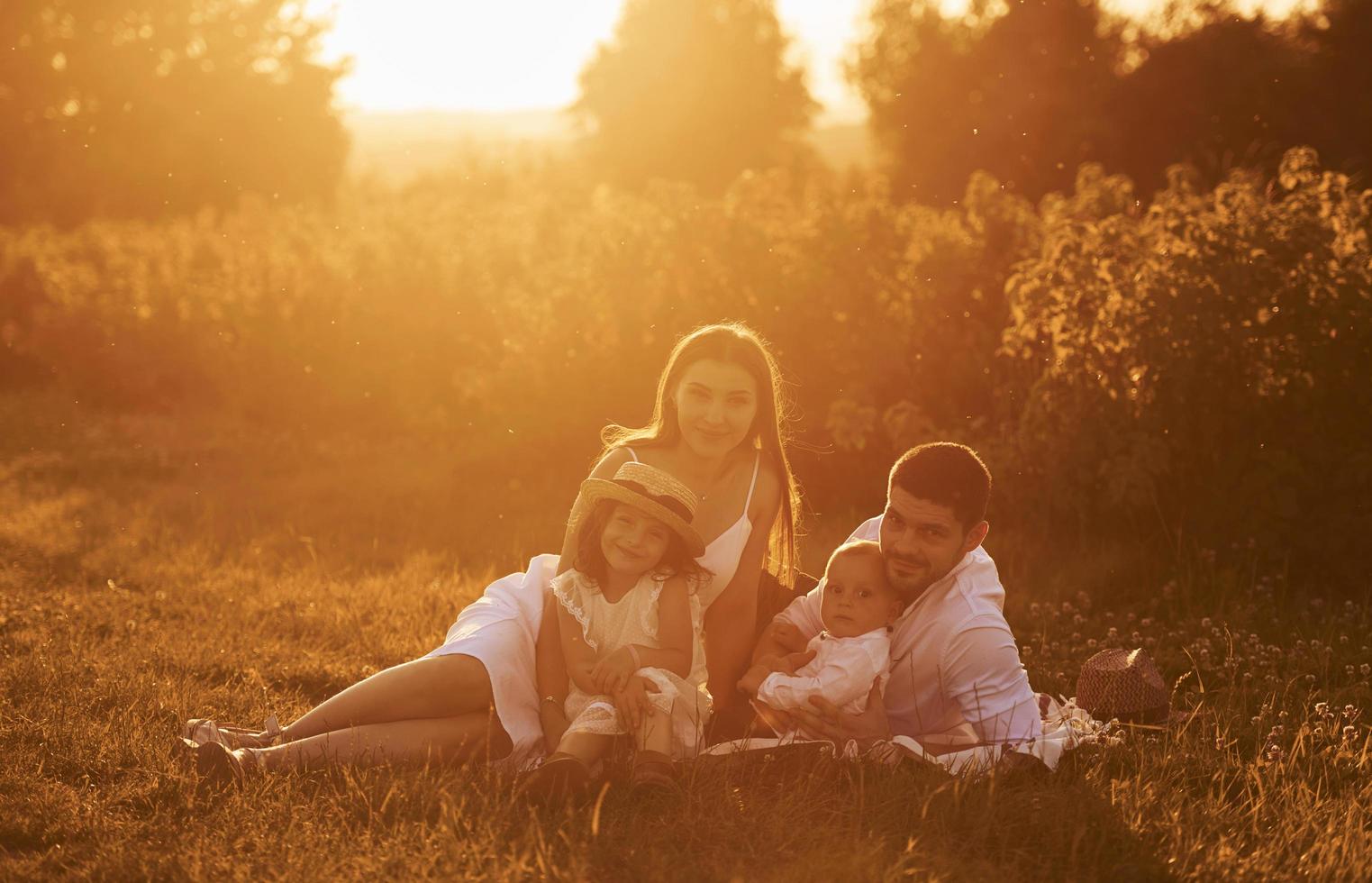 Sitting on the grass. Father, mother with daughter and son spending free time outdoors at sunny day time of summer photo