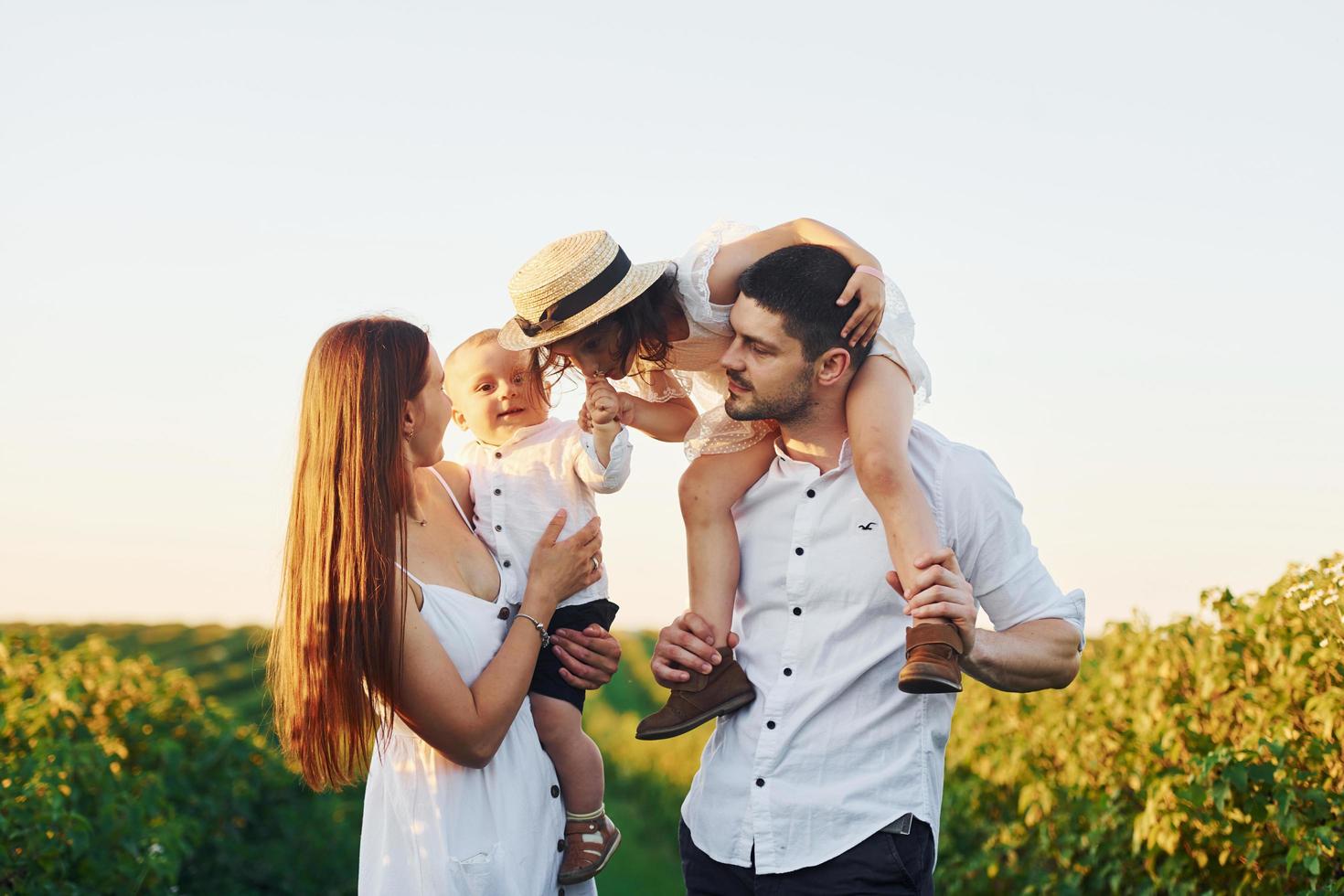 At agricultural field. Father, mother with daughter and son spending free time outdoors at sunny day time of summer photo