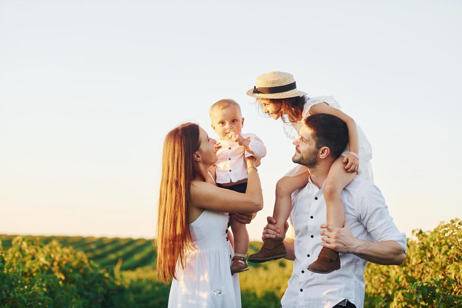 At agricultural field. Father, mother with daughter and son spending free time outdoors at sunny day time of summer photo