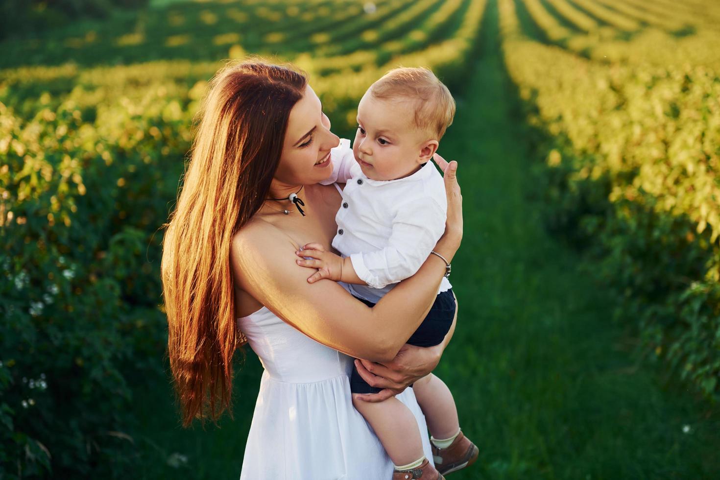 Positive mother with her son spending free time on the field at sunny day time of summer photo