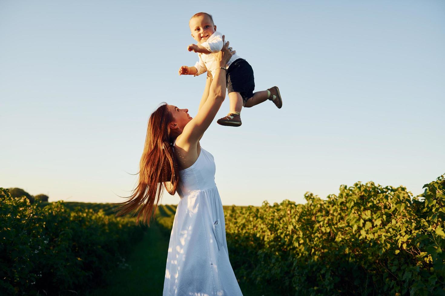 Positive mother with her son spending free time on the field at sunny day time of summer photo