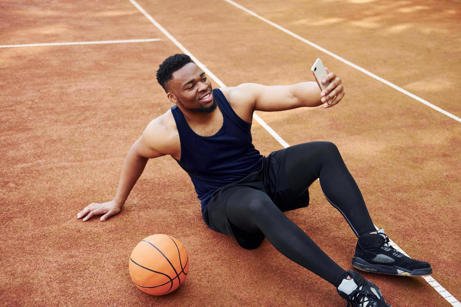 Making selfie. African american man plays basketball on the court outdoors photo