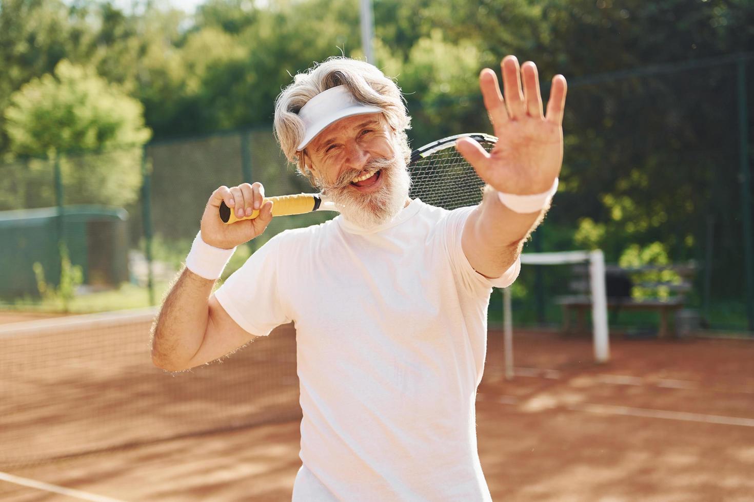 Senior modern stylish man with racket outdoors on tennis court at daytime photo