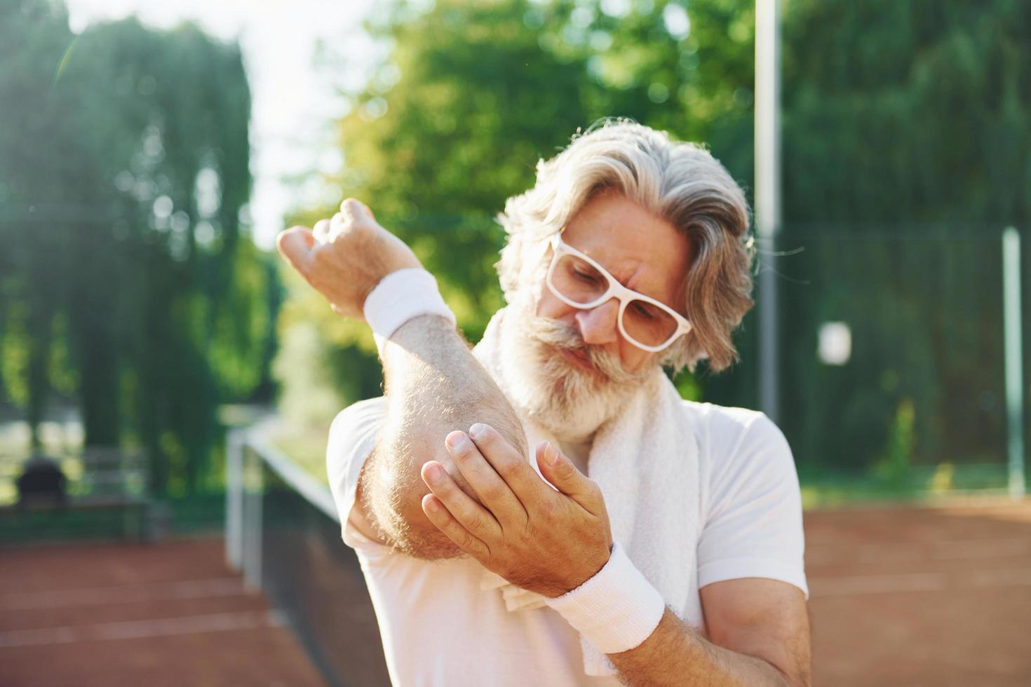 Feeling pain because of trauma. Senior modern stylish man outdoors on the sportive field at daytime photo