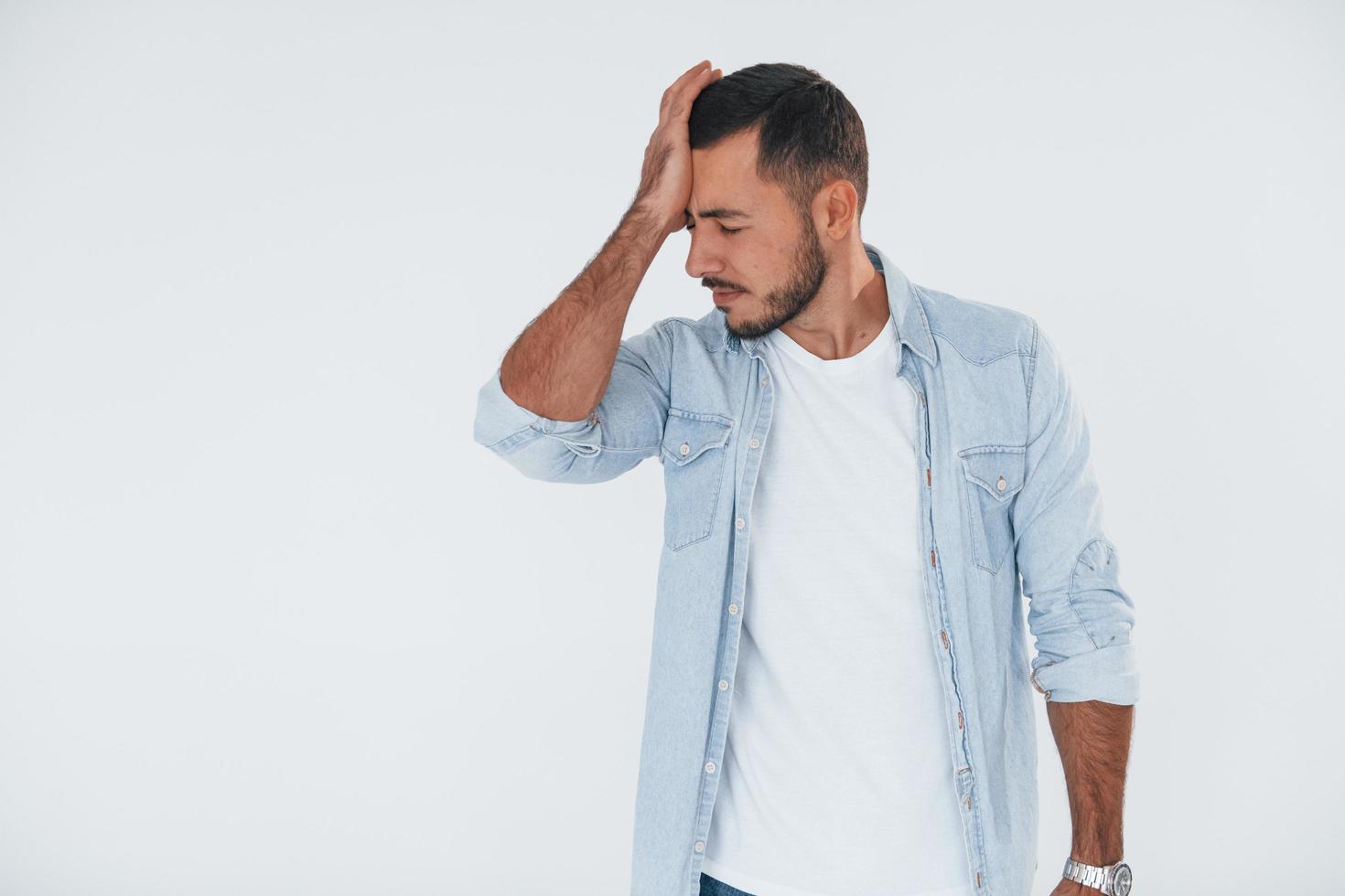 Feels bad. Young handsome man standing indoors against white background photo