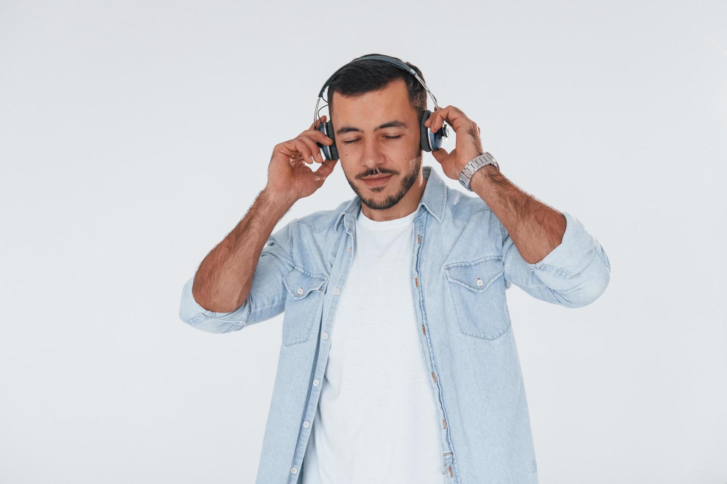 escucha la música en los auriculares. joven apuesto hombre de pie en el interior contra el fondo blanco foto