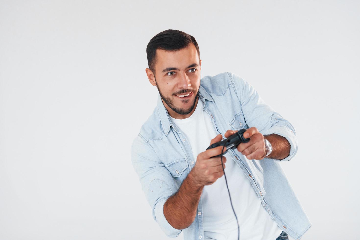 Holds joystick in hands. Young handsome man standing indoors against white background photo
