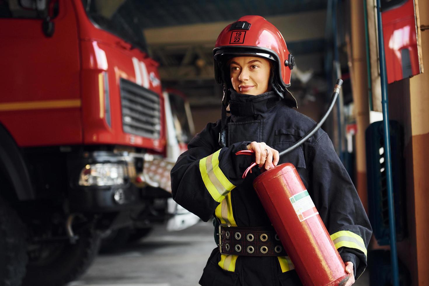 tiene extintor en las manos. bombero femenino en uniforme protector de pie cerca de camión foto