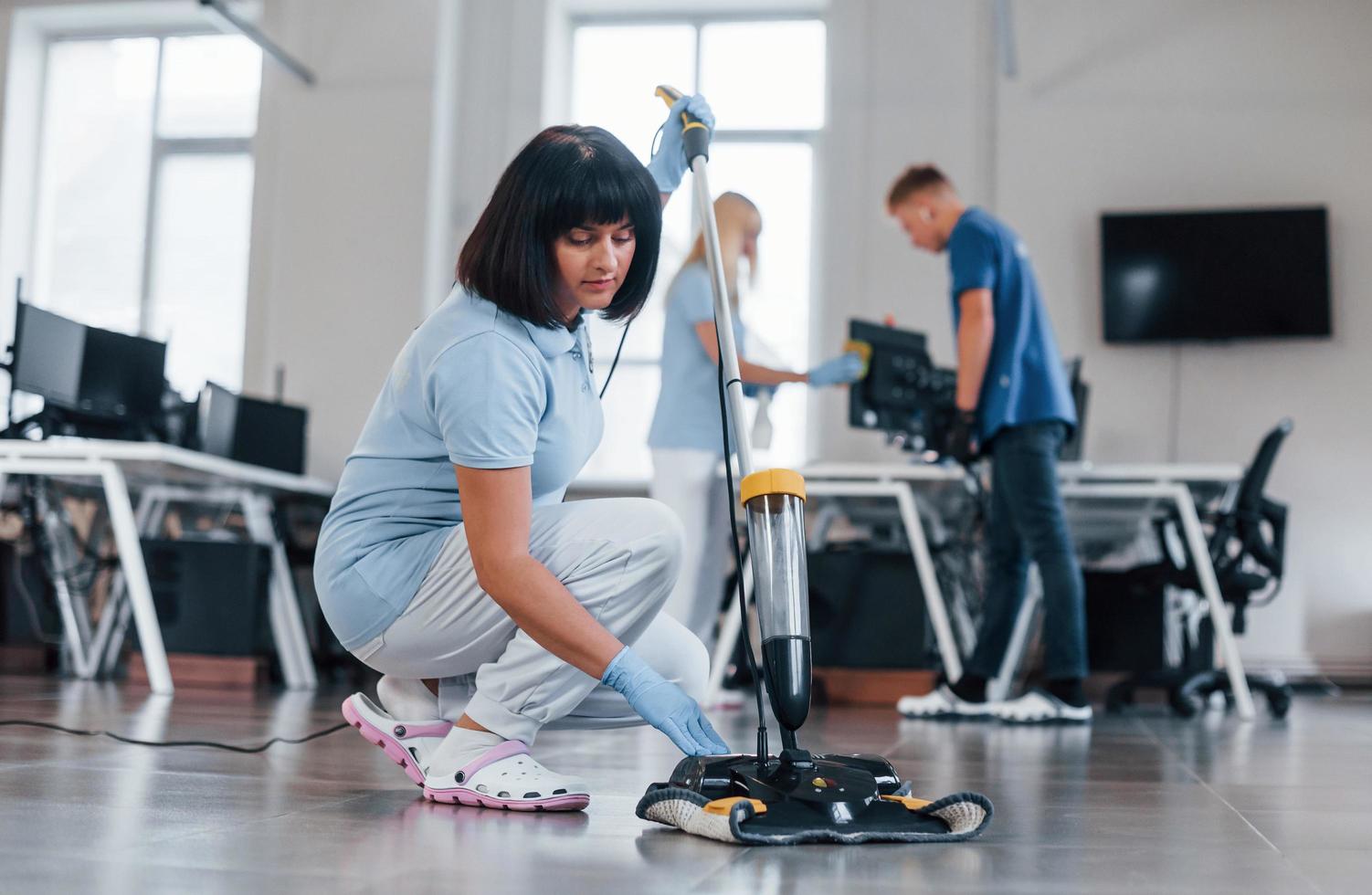 Woman uses vacuum cleaner. Group of workers clean modern office together at daytime photo