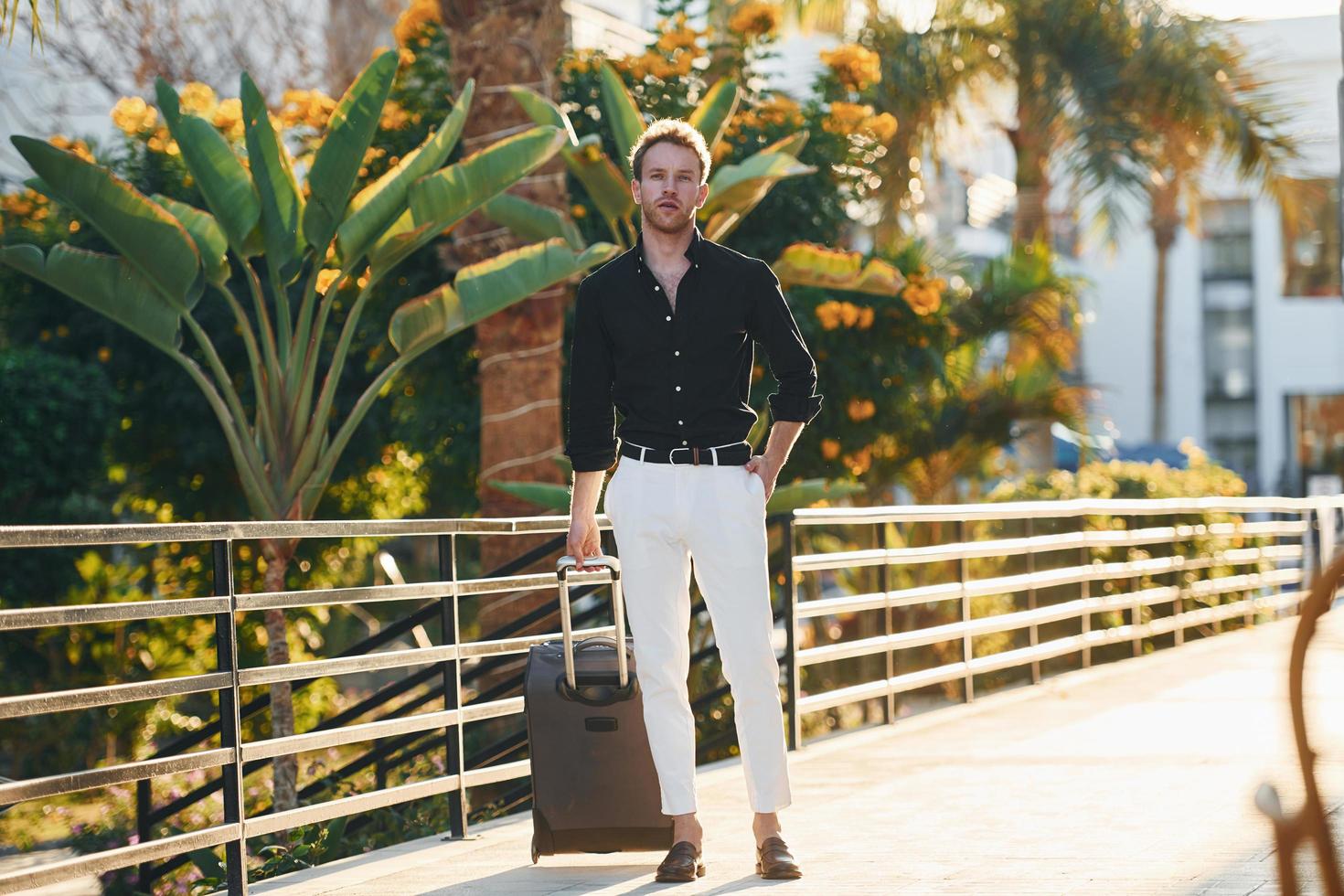 With travel bag. Young man is outdoors at sunny daytime. Concept of vacation photo