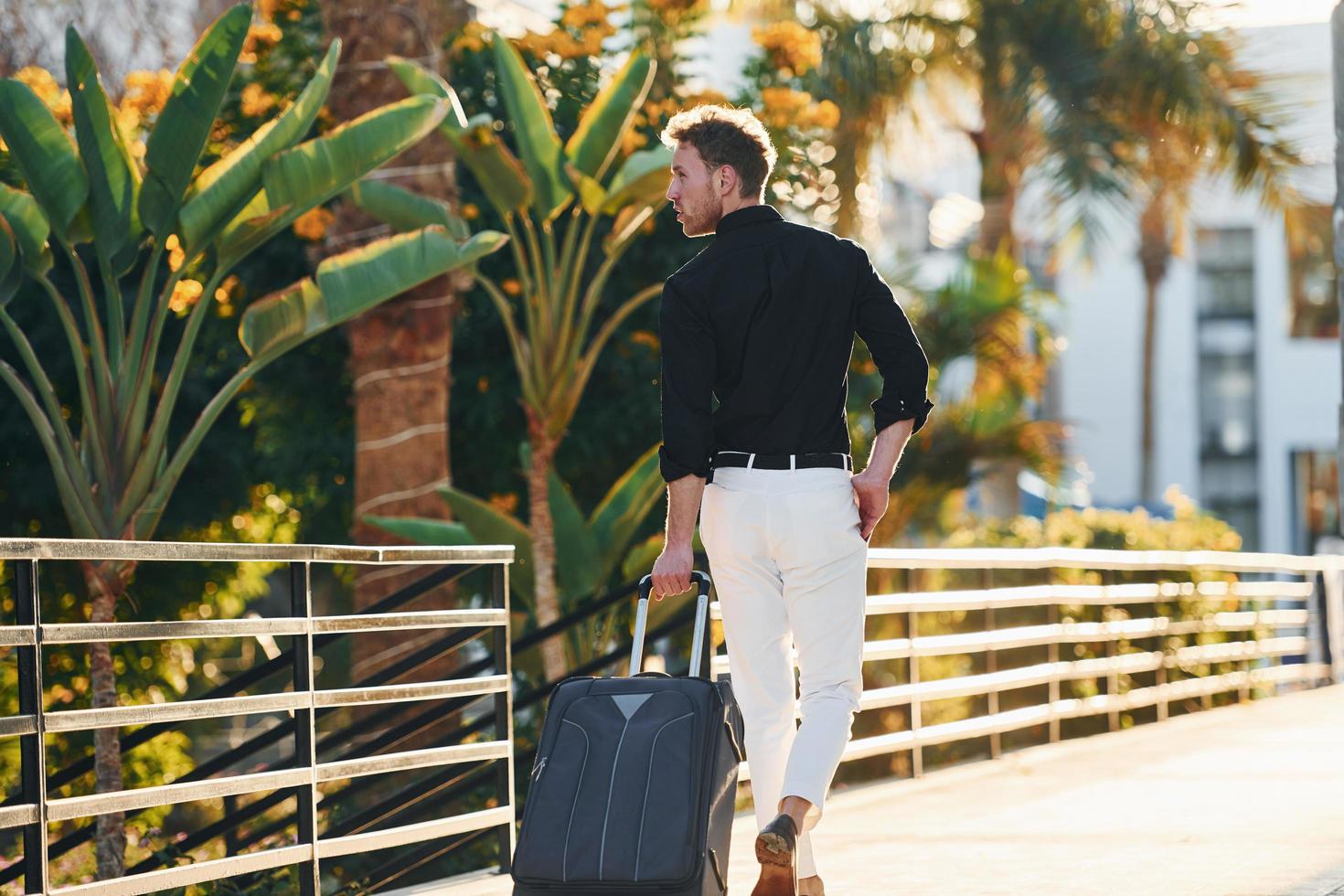 With travel bag. Young man is outdoors at sunny daytime. Concept of vacation photo