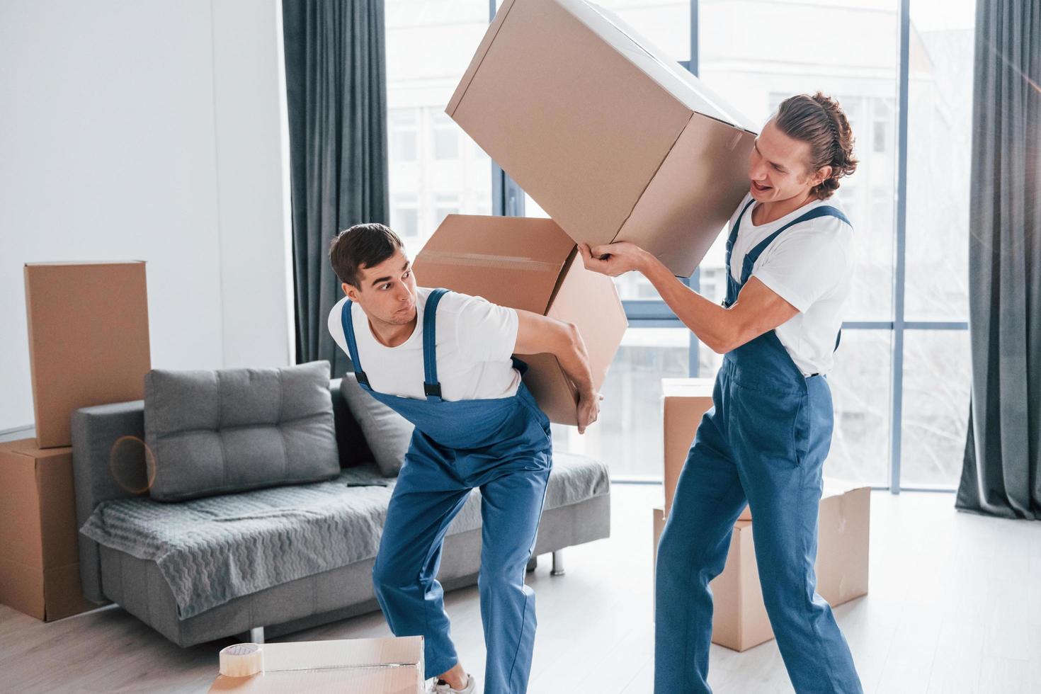 Heavy boxes. Two young movers in blue uniform working indoors in the room photo