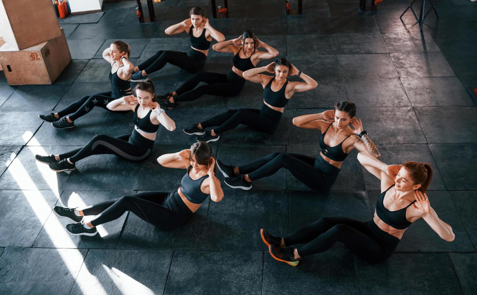 Doing abs. Group of young sportive people have crossfit day indoors in gym photo