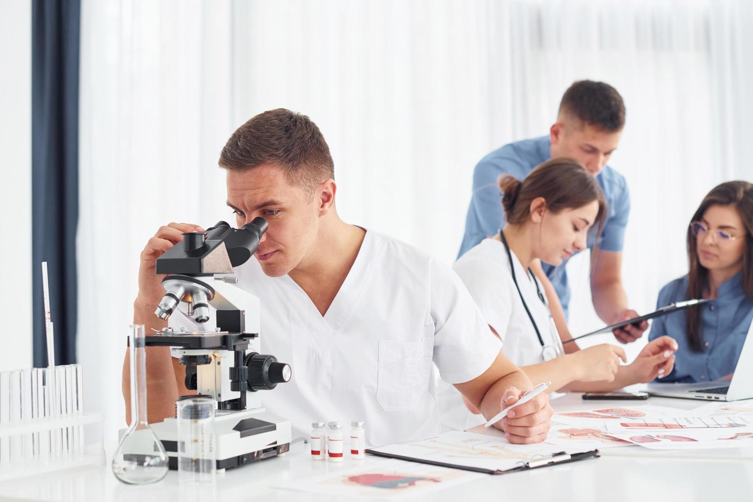 utilizando microscopio. grupo de médicos jóvenes está trabajando juntos en la oficina moderna foto