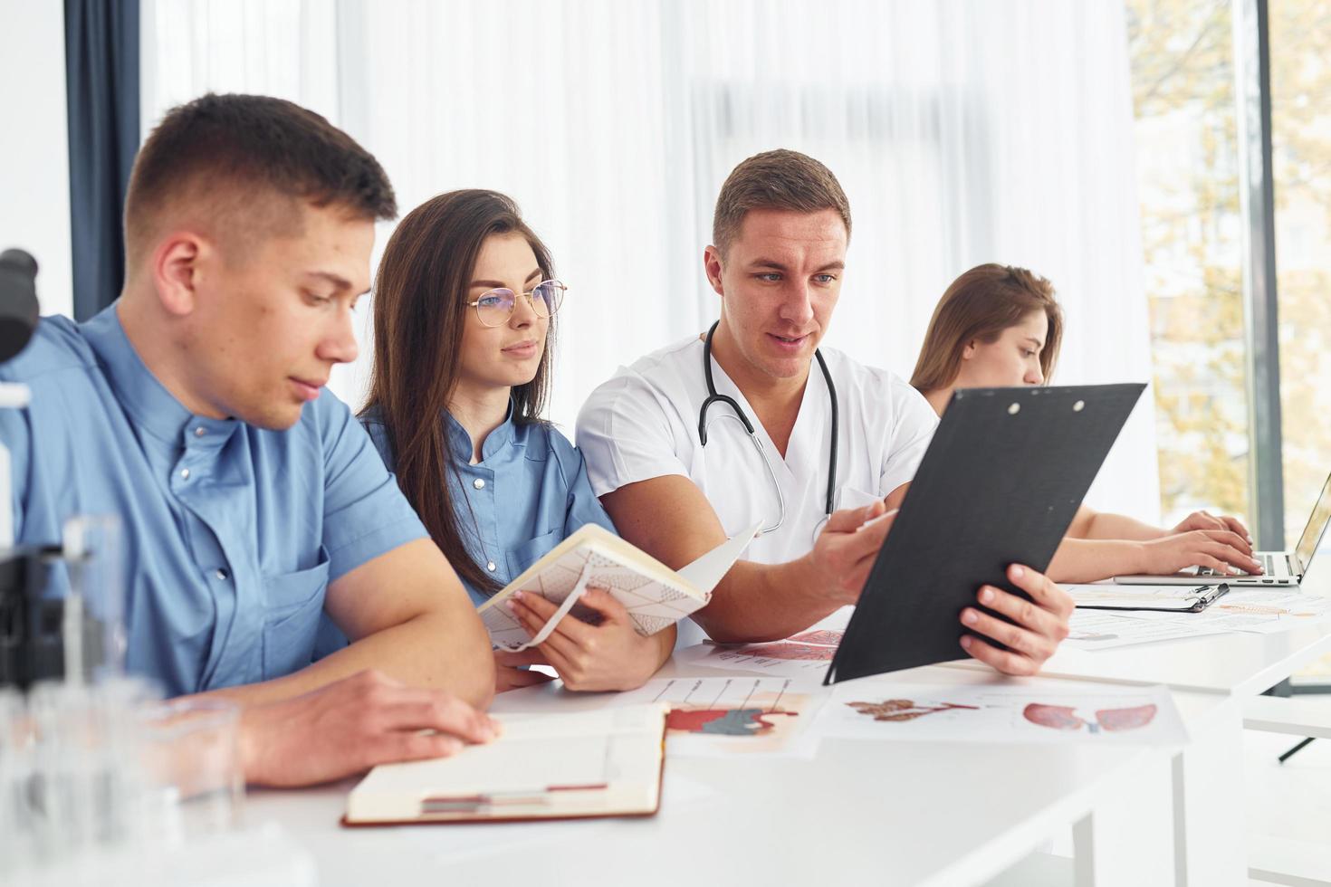 Sitting by the table. Group of young doctors is working together in the modern office photo