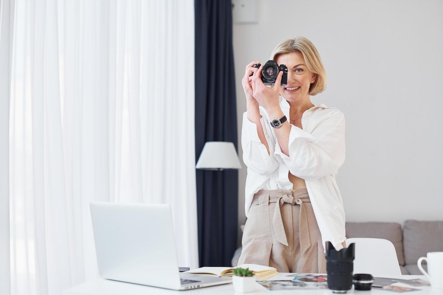Middle-aged woman in elegant clothes is at home. Photographer with camera photo