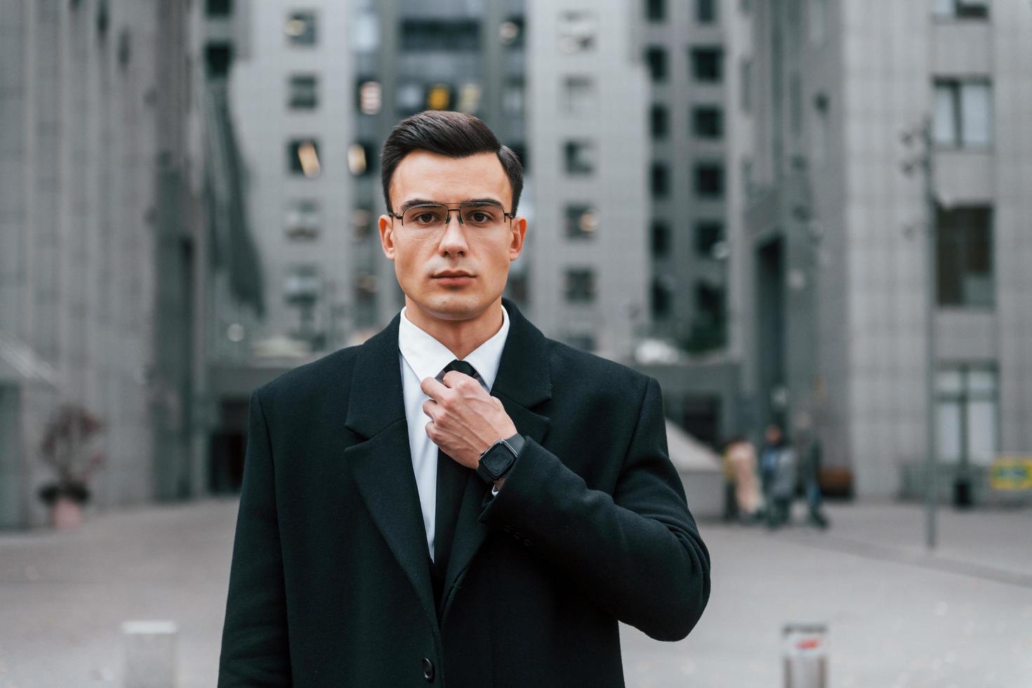 arreglando la corbata. hombre de negocios en traje negro está al aire libre en la ciudad foto