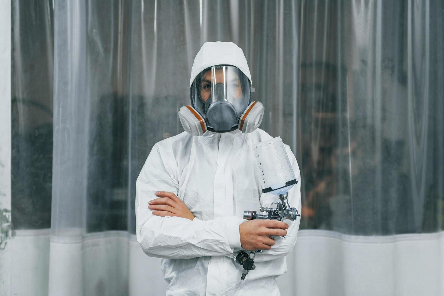 In protective white uniform. Man is working in the auto service photo