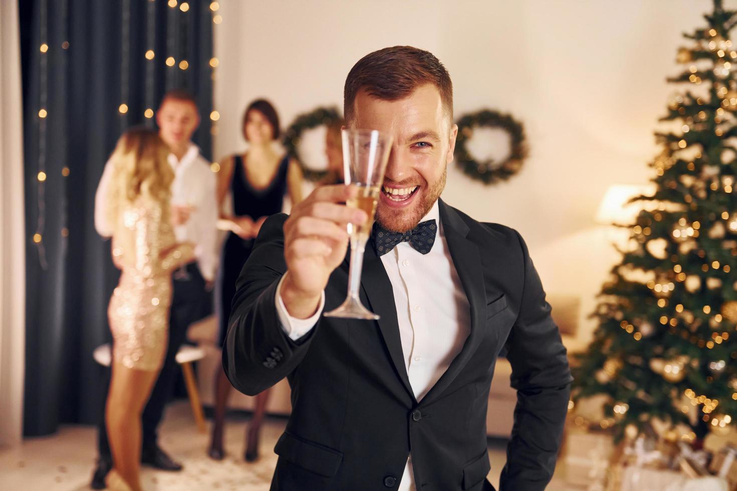 Man with glass of champagne is cheering. Group of people have a new year party indoors together photo