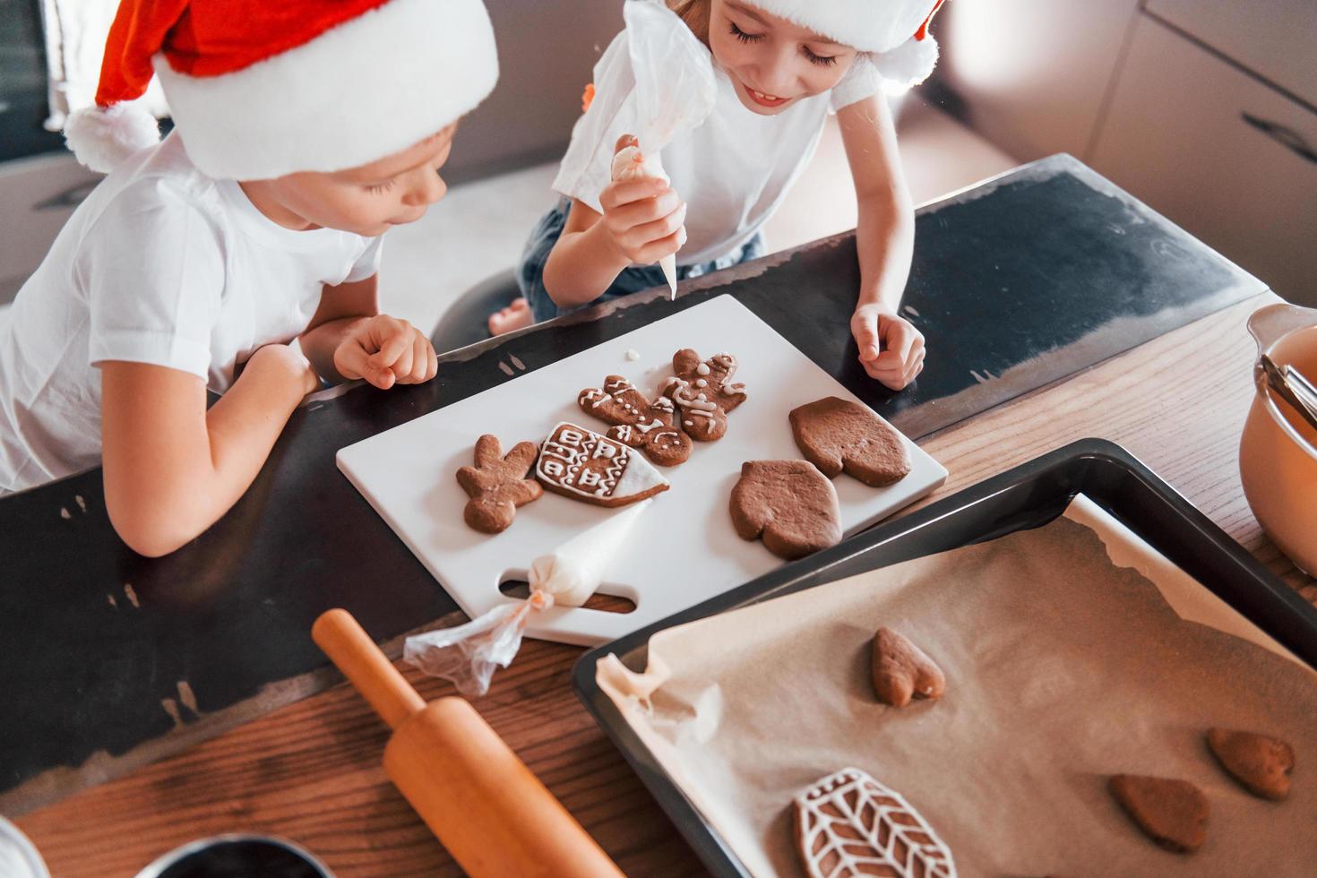 en sombreros de santa. niño y niña preparando galletas navideñas en la cocina foto