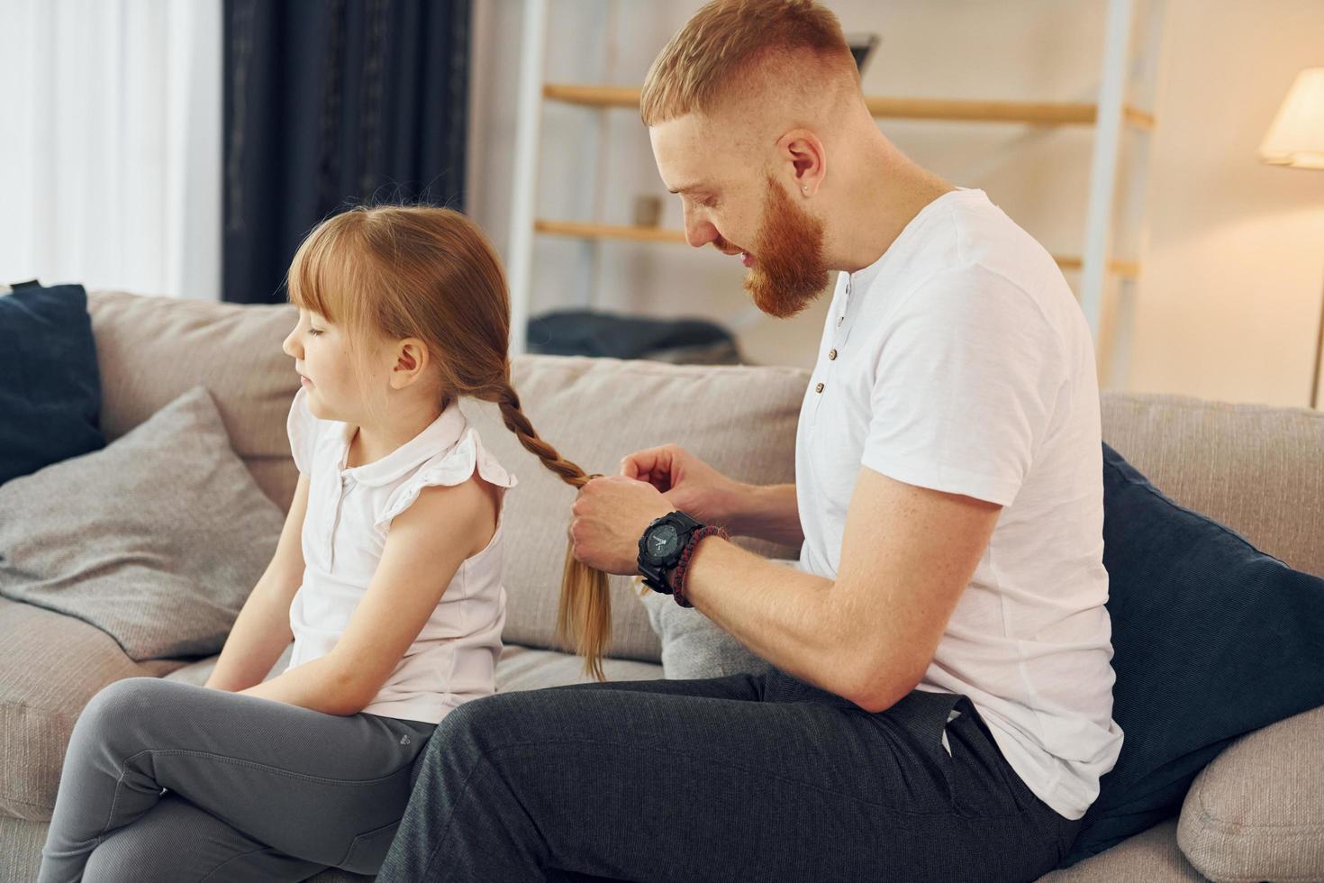 el hombre trenza las trenzas. padre con su pequeña hija está en casa juntos foto