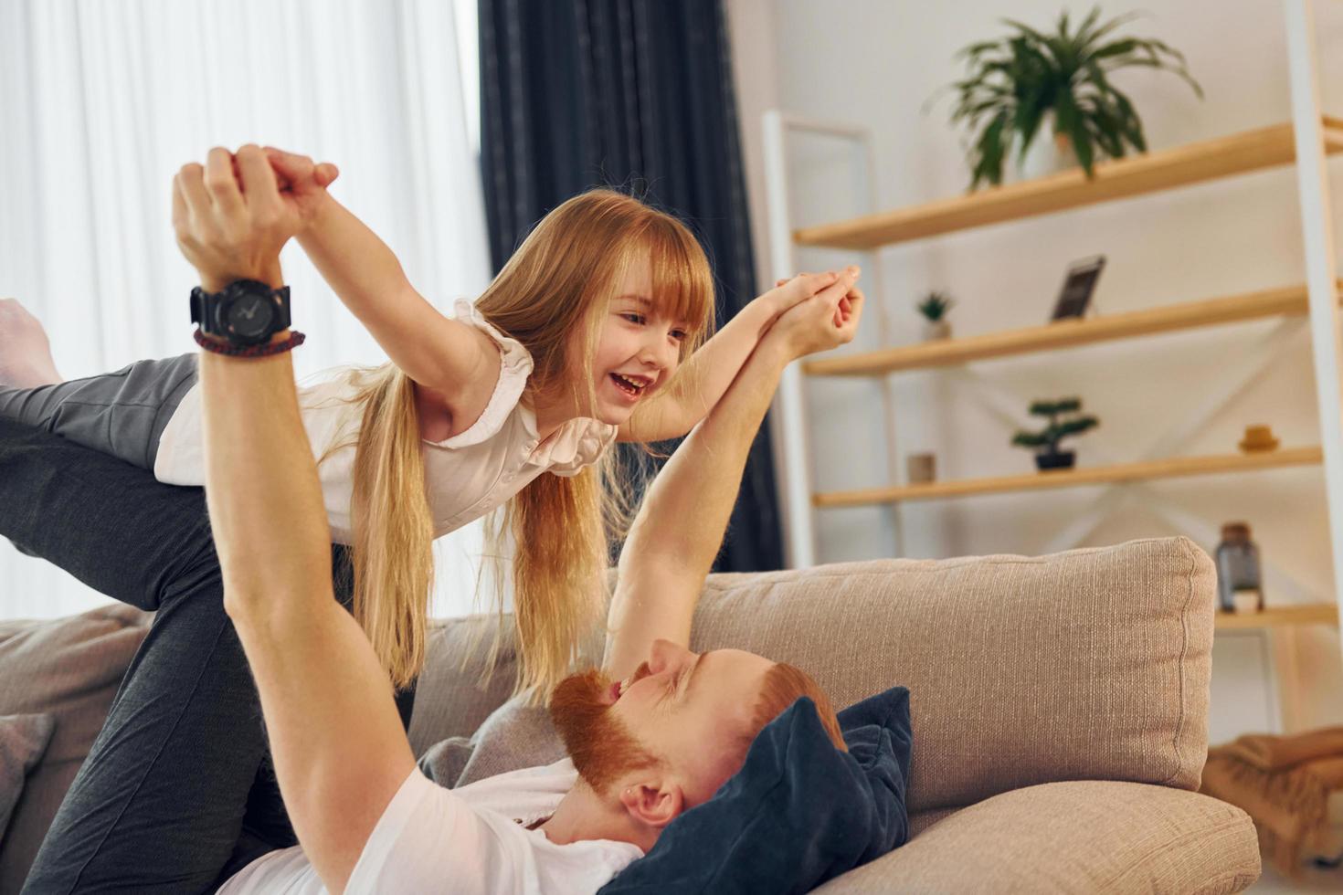 Laying down on the sofa. Father with his little daughter is at home together photo
