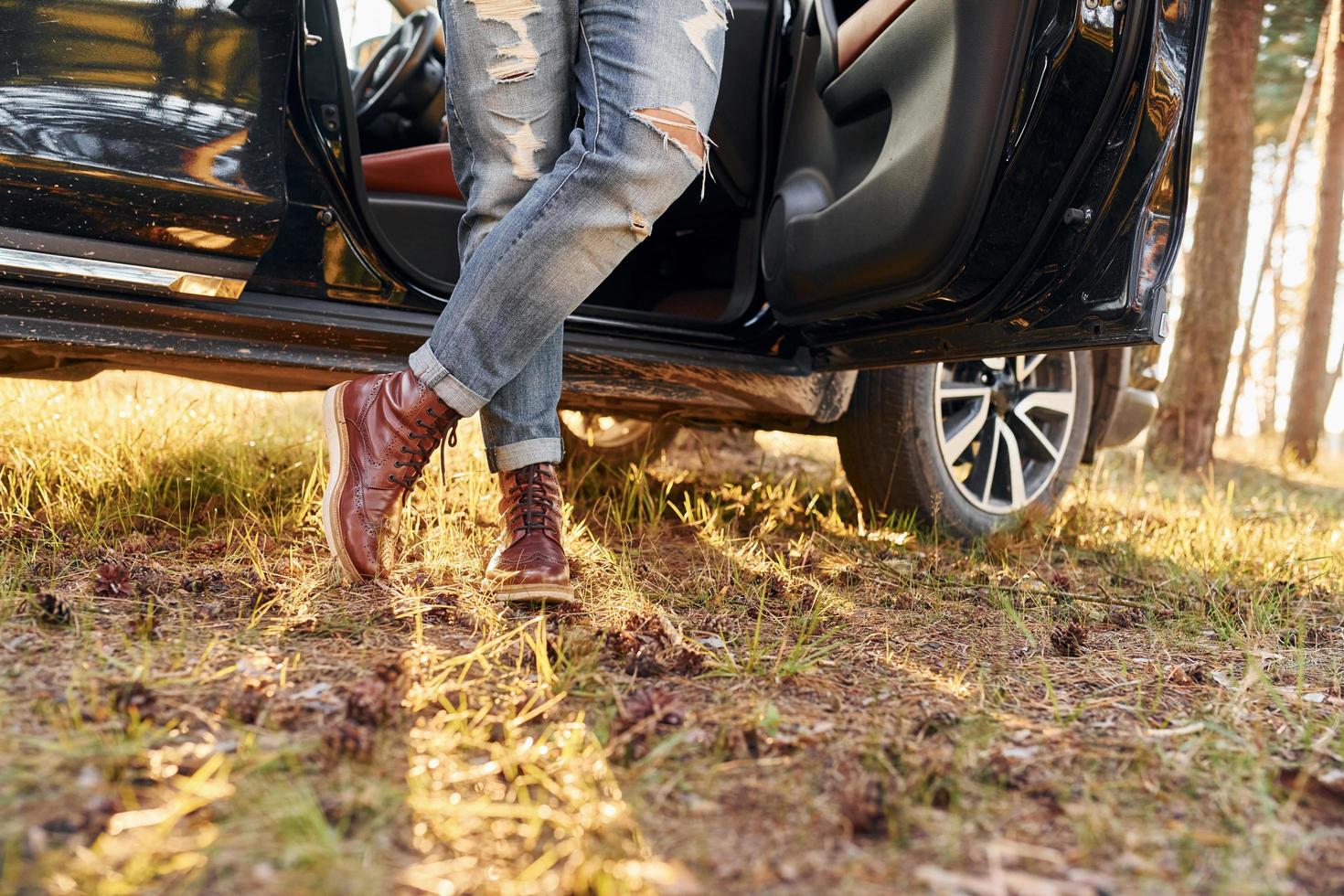 View of jeans and shoes. Man in jeans is outdoors in the forest with his black colored automobile photo