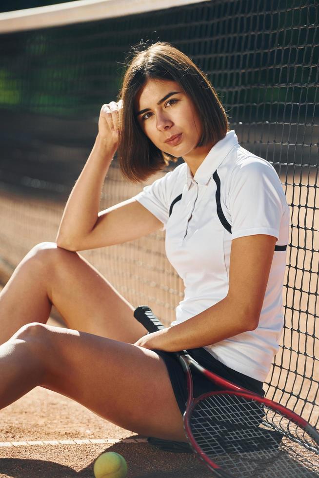 Sitting and holding racket. Female tennis player is on the court at daytime photo