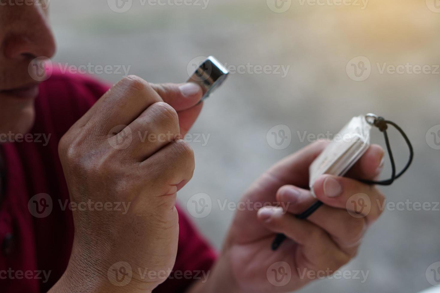 el hombre asiático de primer plano sostiene una pequeña lupa para inspeccionar los detalles y el patrón del amuleto. concepto, fe y creencia en la santidad y la suerte para los budistas. colleting amulet como pasatiempos, intercambio o comercio. foto