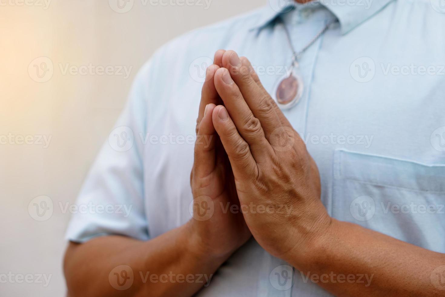 Closeup man in blue shirt ,wears Buddha amulet, praying with hands buddhist pray gesture, Wai in Thai culture. Concept, woreship for lucky, faith and belief. Pattern of respect and greeting. photo