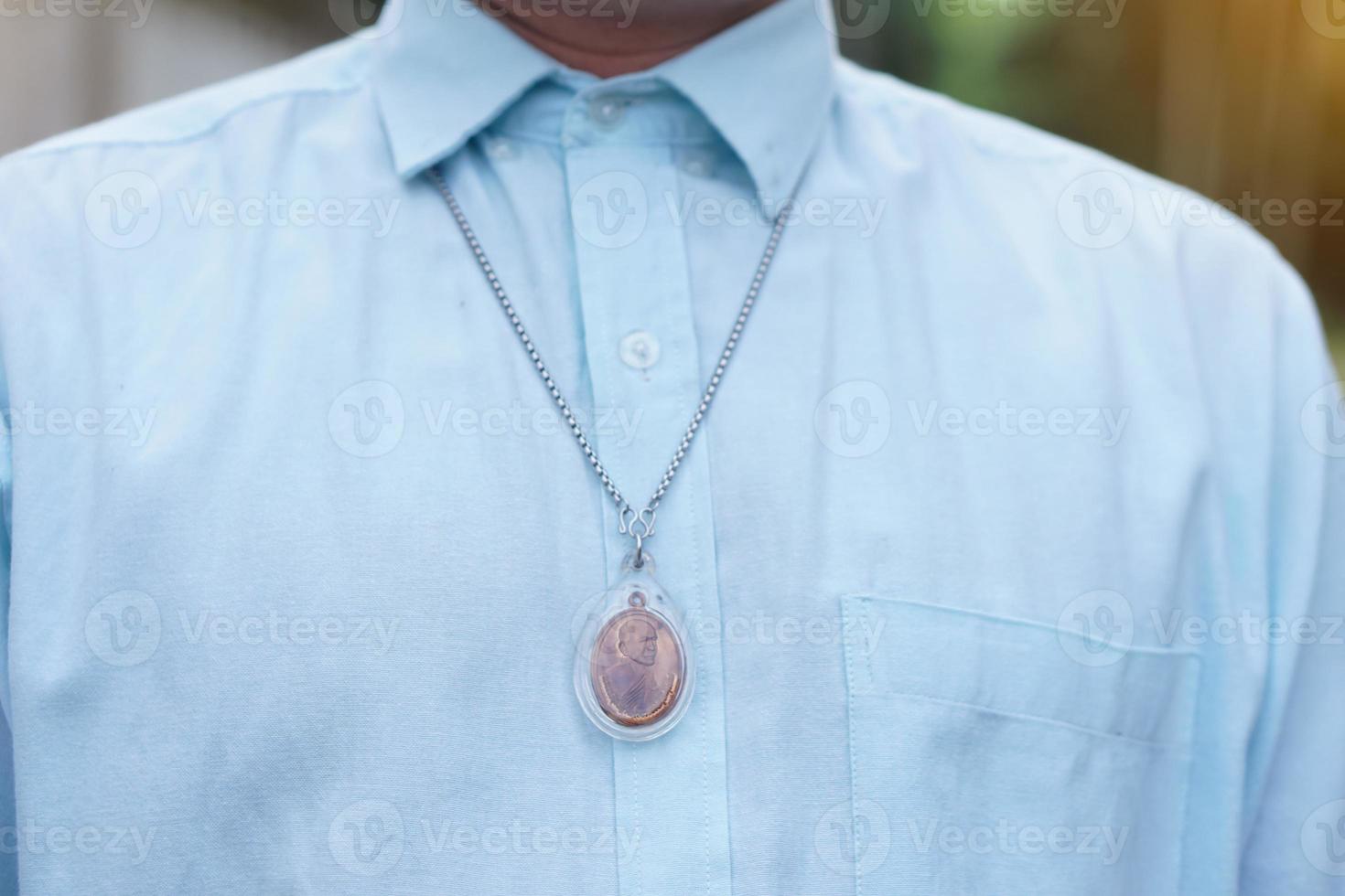 el hombre de primer plano con camisa azul usa un collar de amuleto de buda tailandés. concepto, fe y creencia de los budistas para proteger de los peligros, traer buena suerte, prosperidad comercial y riqueza. foto