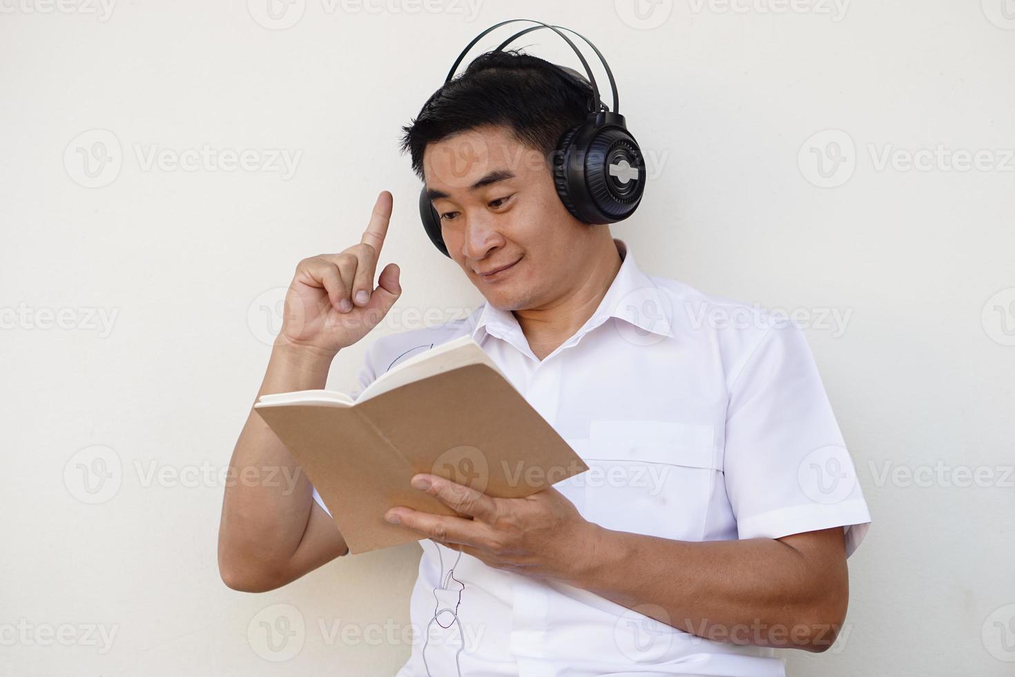 Asian man reads book and wears headphone listen to soft music to make concentration in reading. Get idea. Concept, free time, pastime, hobby, Relax with music. photo
