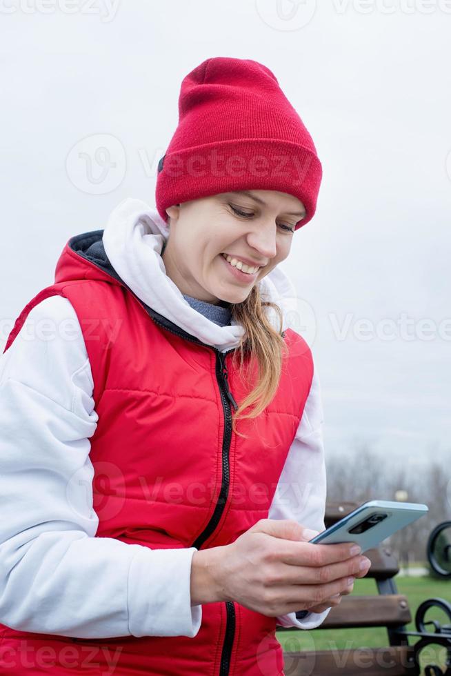 Woman wearing knee brace or orthosis after leg surgery sitting in the park using smartphone photo