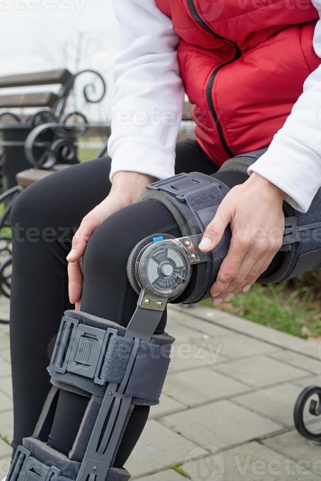 Woman wearing knee brace or orthosis after leg surgery, walking in the park photo