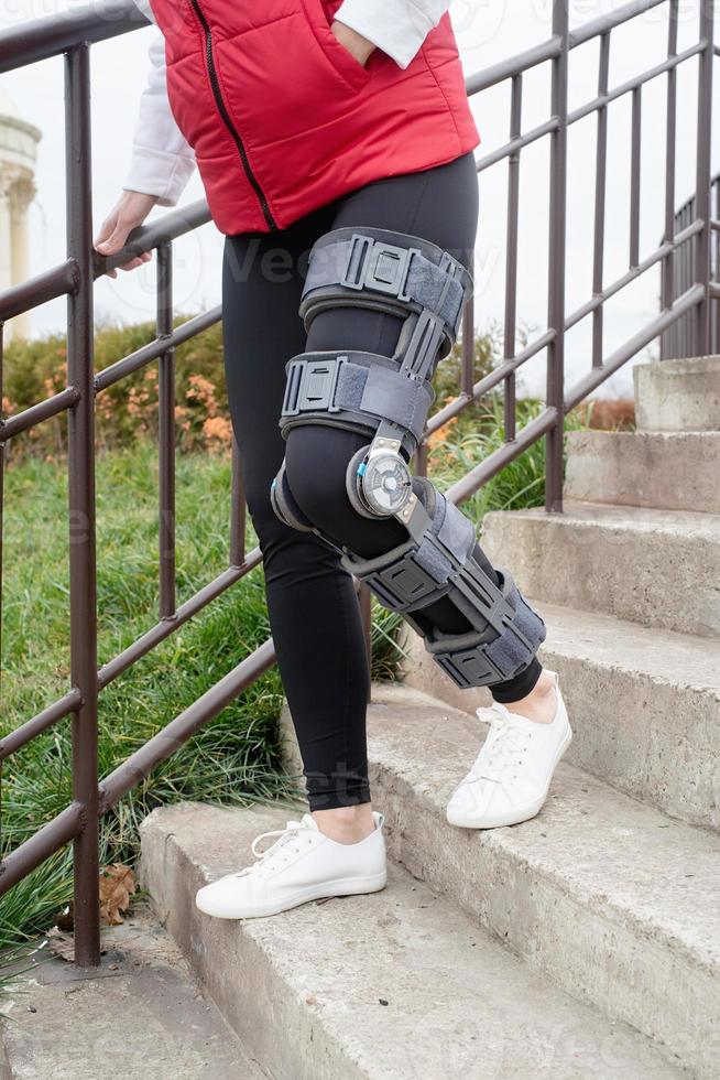 Woman wearing knee brace or orthosis after leg surgery, walking in the park photo