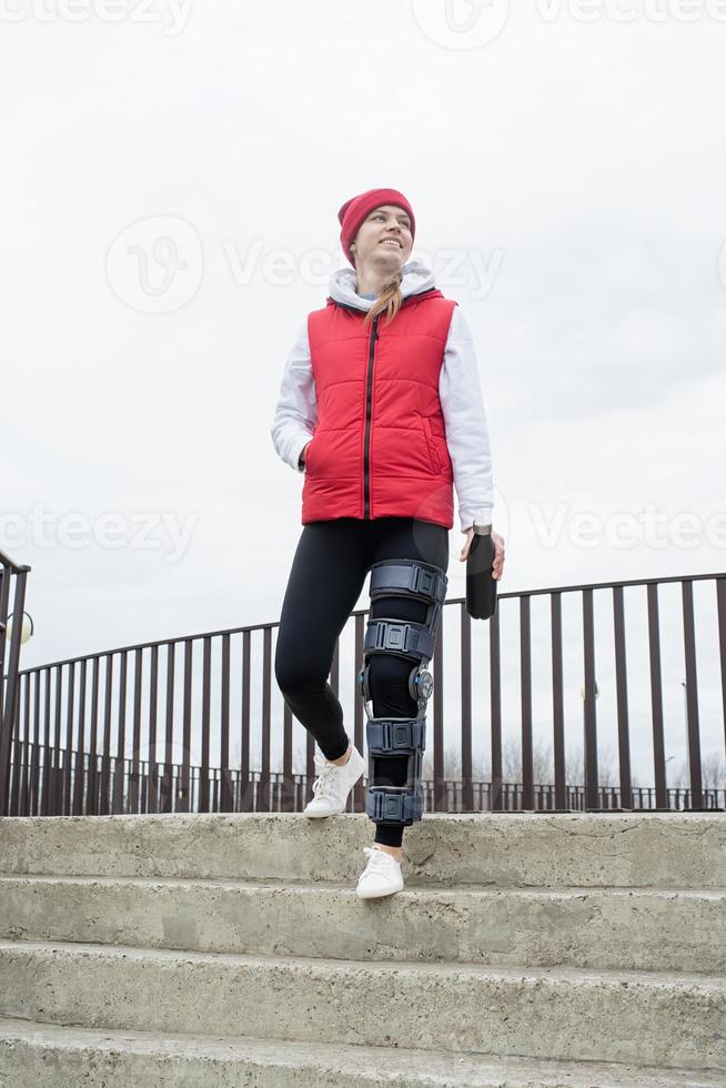 Woman wearing knee brace or orthosis after leg surgery, walking in the park photo