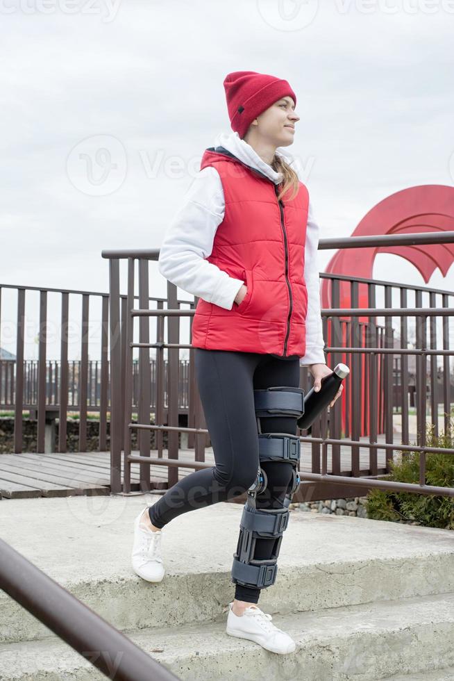 Woman wearing knee brace or orthosis after leg surgery, walking in the park photo