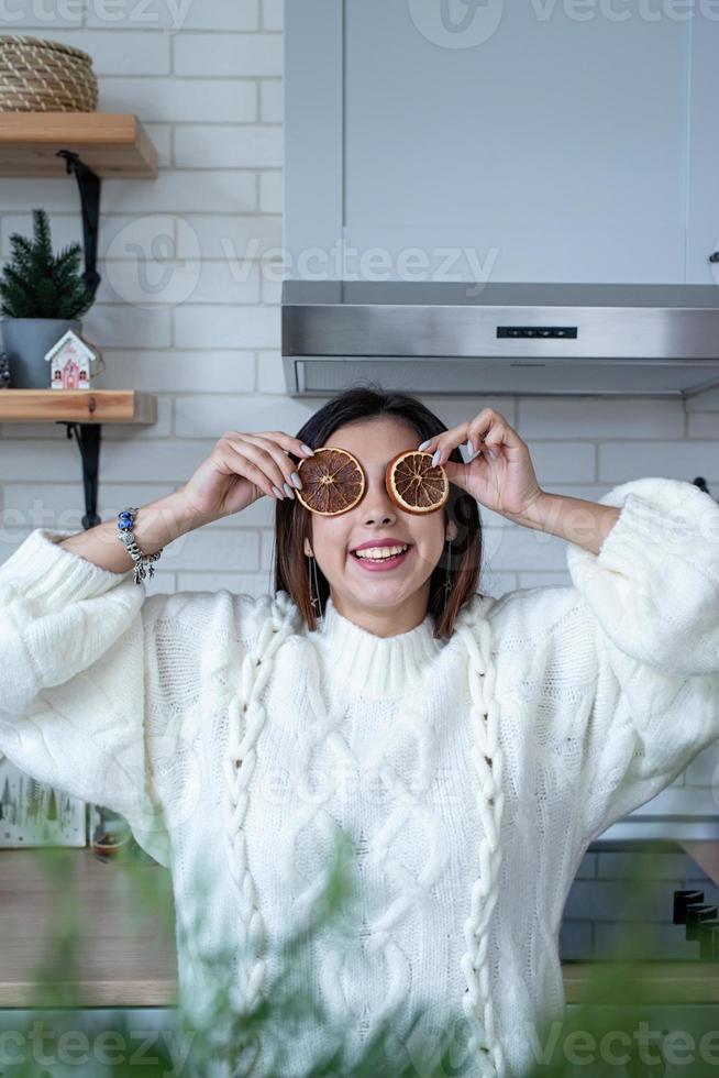 Woman in warm white winter sweater standing at the kitchen at home with dry lemon slices next to face photo