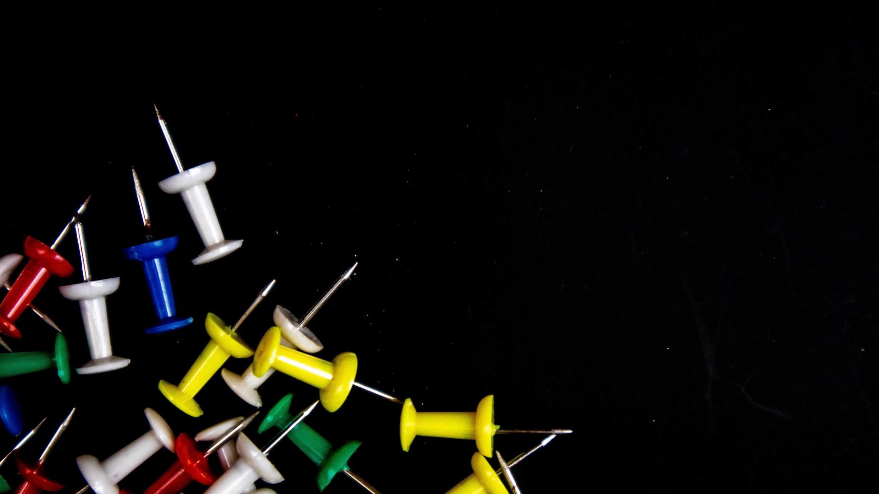 multicolored thumbtacks on a black background photo