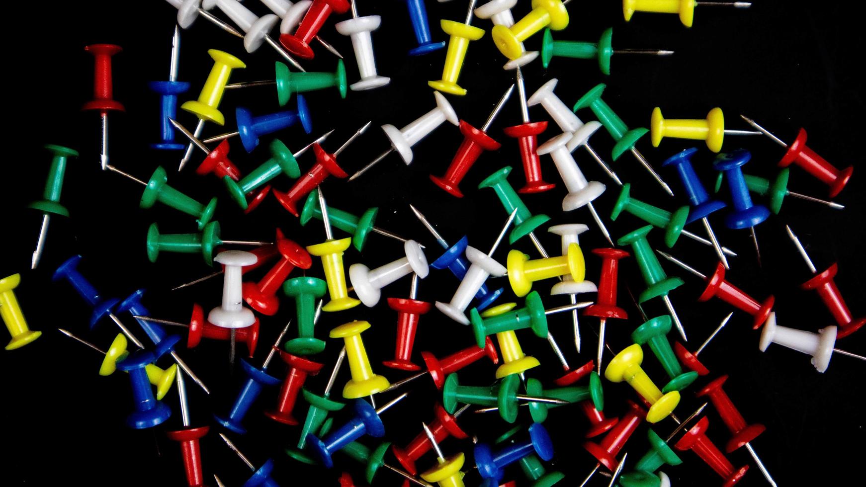 multicolored thumbtacks on a black background photo