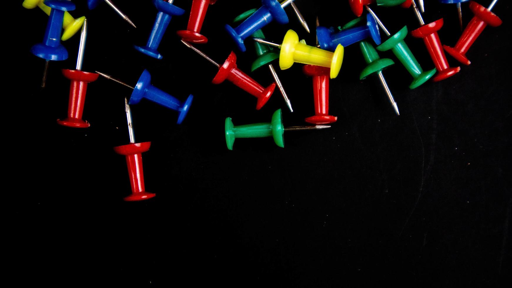 multicolored thumbtacks on a black background photo