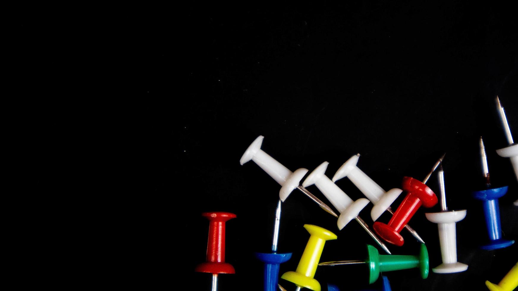 multicolored thumbtacks on a black background photo