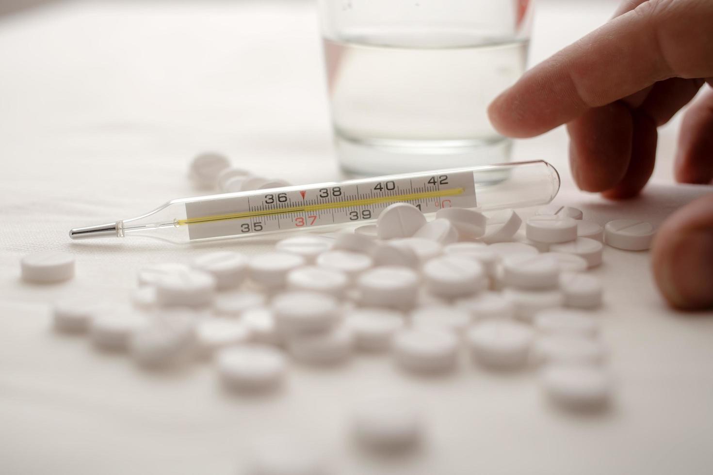 Medical thermometer, with a temperature of 37 degrees in a pile of pills, against the background of a hand and a glass of water. photo