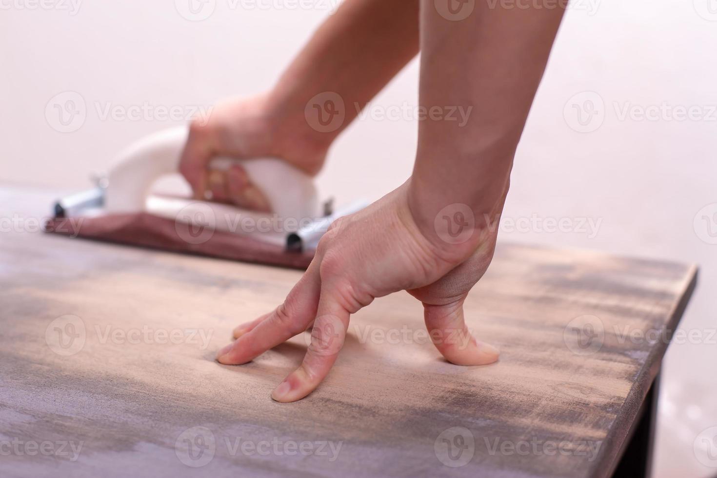 Hand with a carpentry holder for sandpaper erases and polishes an old wooden surface, prepares for painting. Home repairs. photo