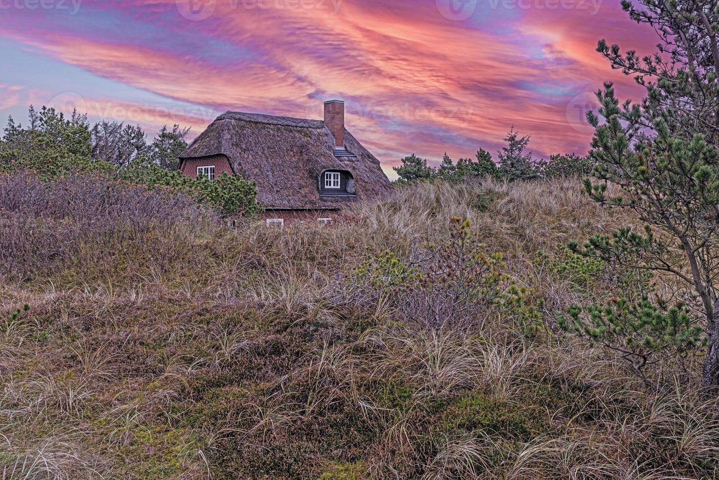 imagen de una casa con techo de paja en las dunas de la costa del mar del norte de Dinamarca al atardecer foto