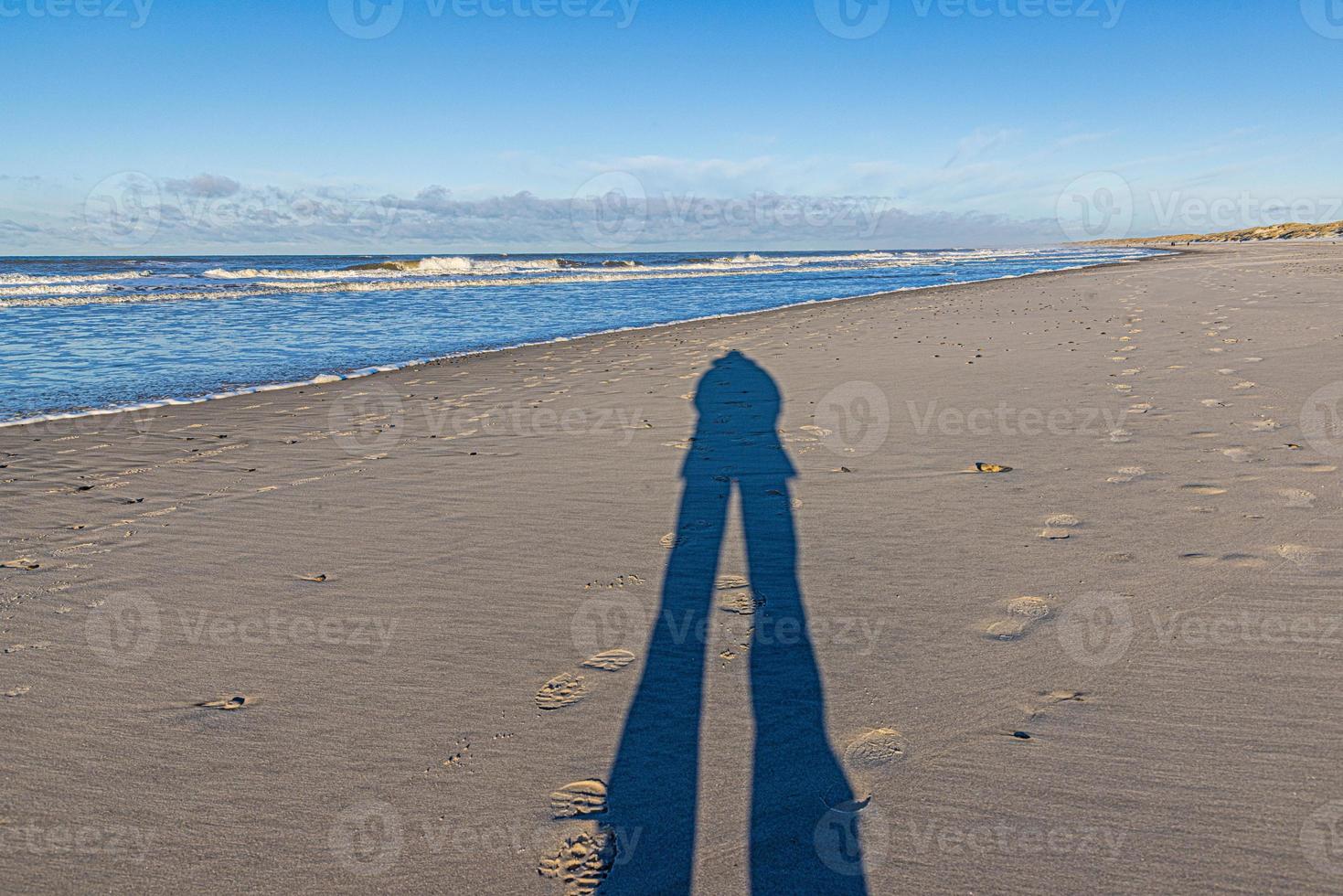 Image of a long shadow of a person on a wide sandy beach photo