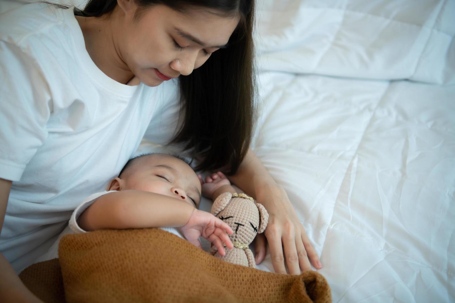 Young mother hugging her newborn child to lull the baby to sleep in the white bedroom photo